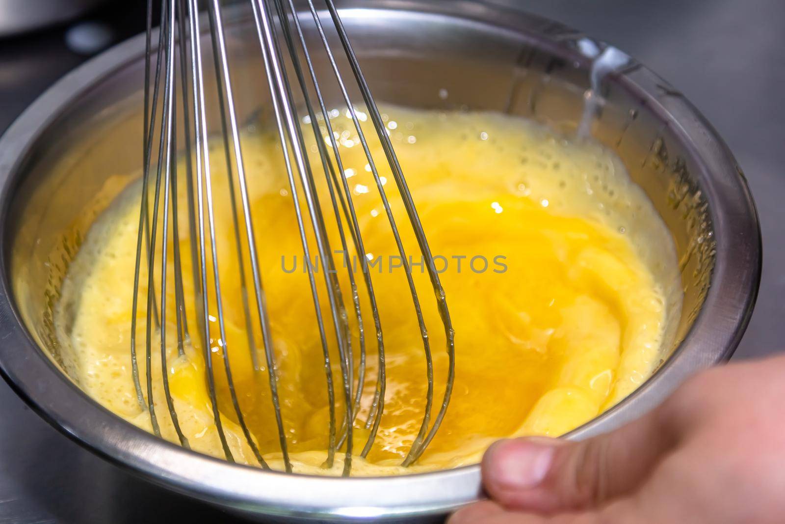 whisking egg yolks and sugar in a bowl by Milanchikov