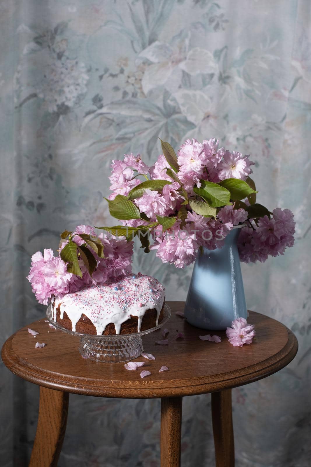 Easter cake and painted eggs and a bouquet of pink sakura flowers on a table in a decorated spring room, a beautiful still life. High quality photo