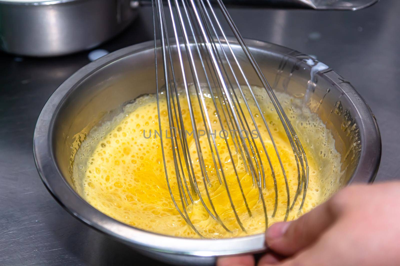 whisking egg yolks and sugar in a bowl by Milanchikov