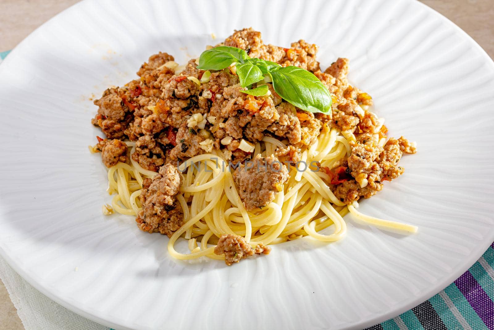 Rich spicy Italian spaghetti Bolognaise with parmesan cheese and a fresh green basil leaves viewed from overhead on a white plate in square format.