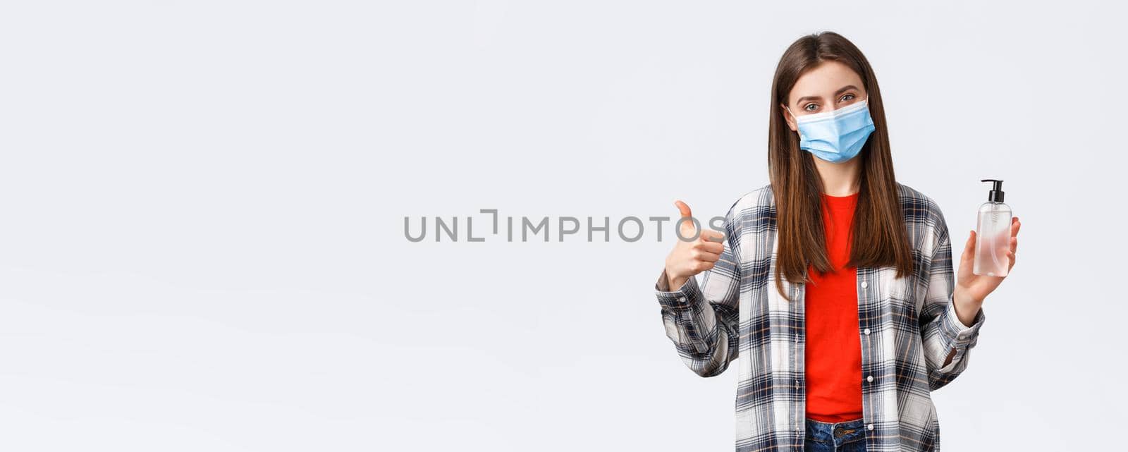 Coronavirus outbreak, leisure on quarantine, social distancing and emotions concept. Cheerful pleased young girl recommend hand-sanitizer brand, thumb-up, wear medical mask by Benzoix