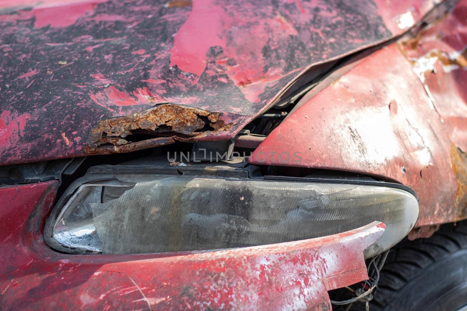 Broken headlights as a result of a collision. Broken red car after an accident. Car accident concept. Damaged emergency headlight, hood and bumper. Damage to the car body after the accident