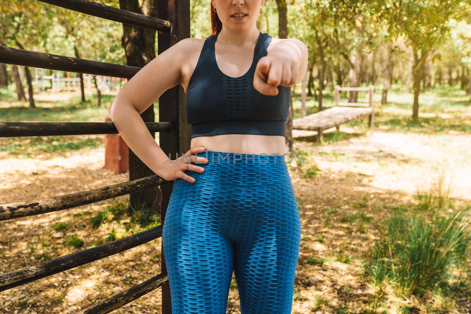 young female athlete pointing her index finger at the camera outside. young girl athlete challenging the viewer. health and wellness lifestyle. outdoor public park, natural sunlight.