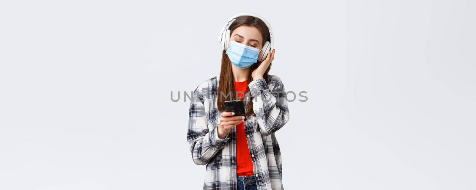 Social distancing, leisure and lifestyle on covid-19 outbreak, coronavirus concept. Carefree and relaxed woman in medical mask, close eyes enjoying music in headphones, hold mobile phone by Benzoix