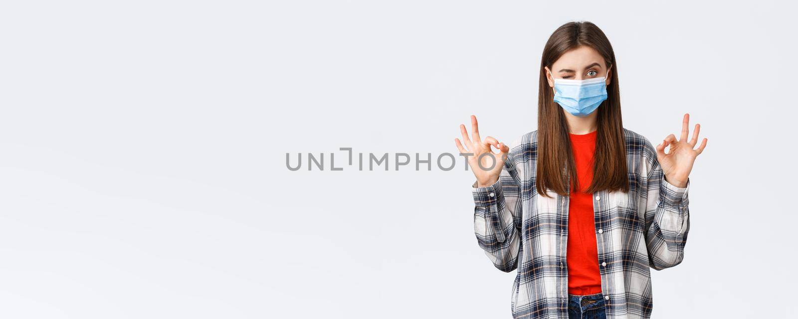 Coronavirus outbreak, leisure on quarantine, social distancing and emotions concept. Determined young woman in medical mask assure all good, show okay signs and wink, no problem by Benzoix