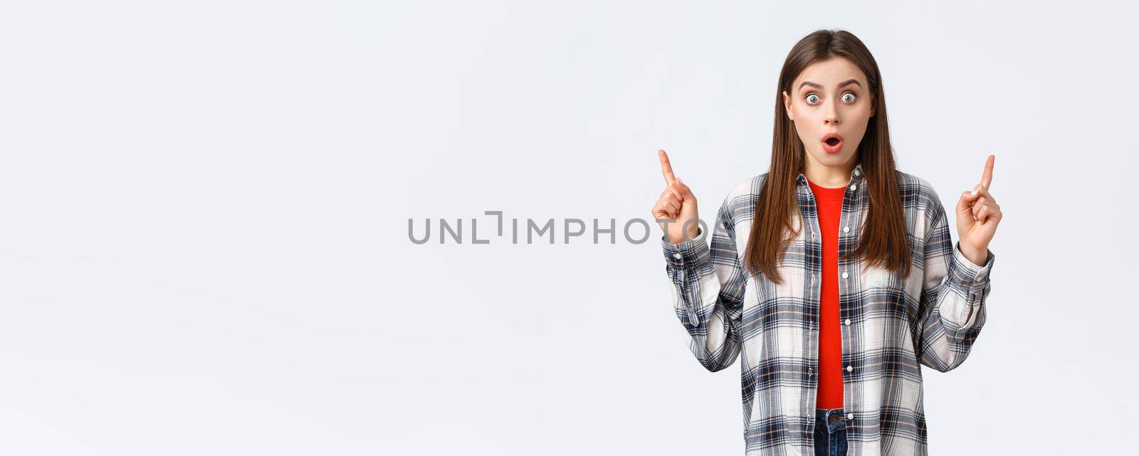 Lifestyle, different emotions, leisure activities concept. Astonished and speechless attractive girl in checked shirt pointing fingers up to tell news, drop jaw staring, make wow expression.
