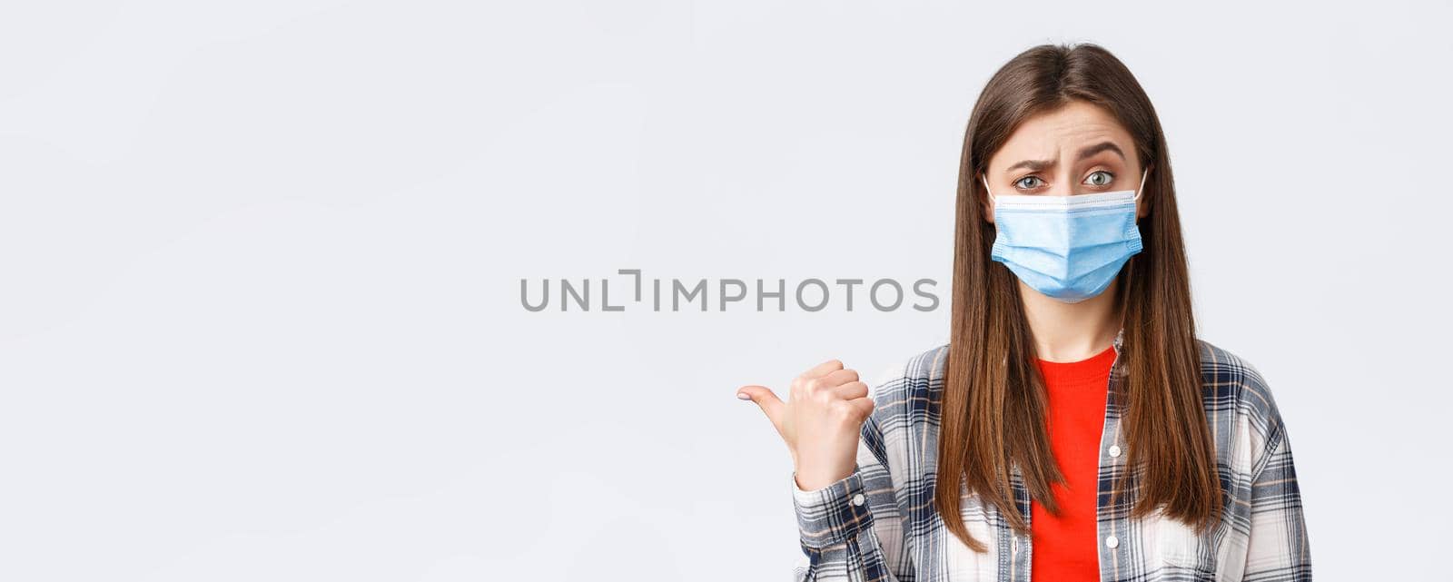 Coronavirus outbreak, leisure on quarantine, social distancing and emotions concept. Skeptical young woman in medical mask express disbelief towards banner to the left, pointing doubtful.