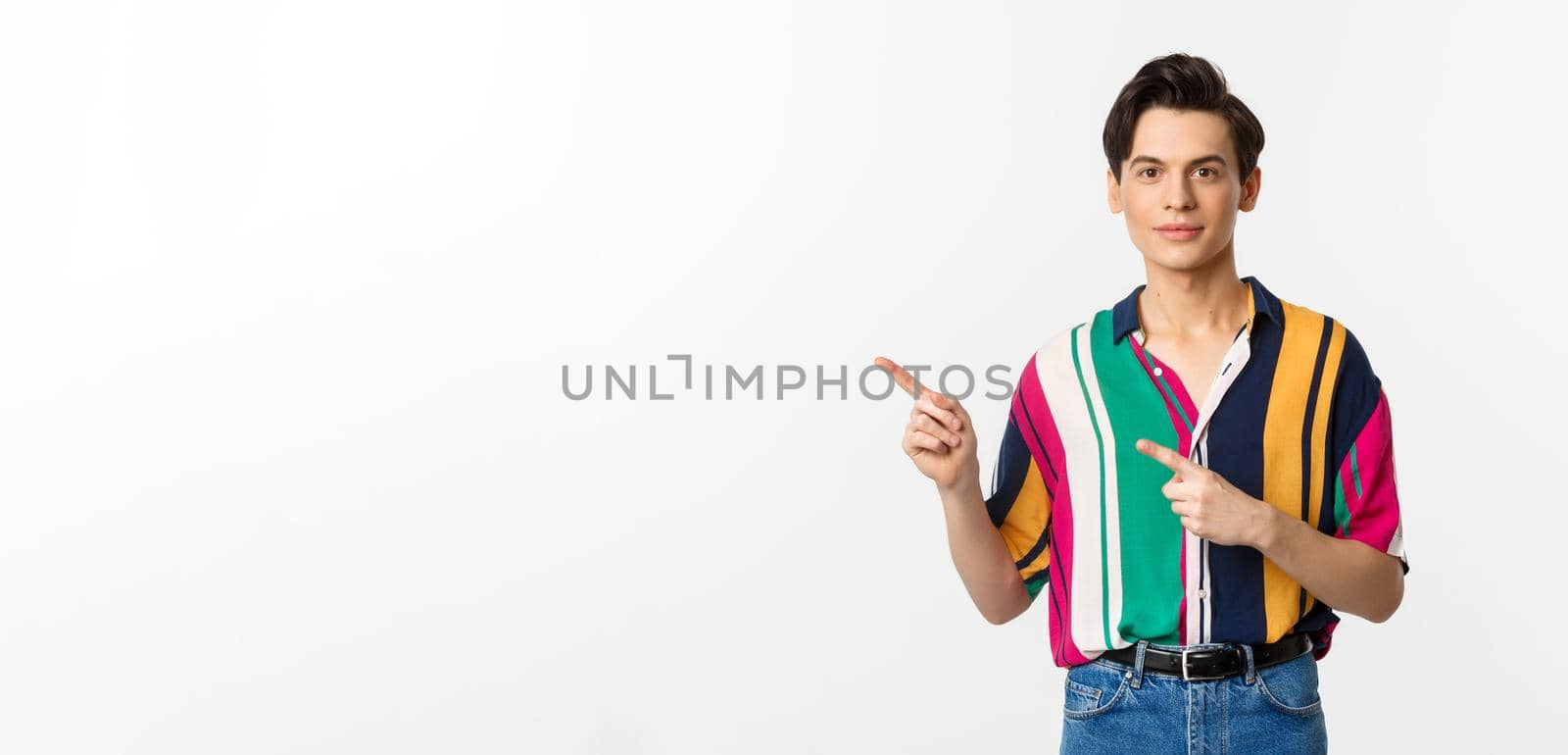 Image of stylish androgynous man smiling, pointing fingers left at logo, showing promo offer, standing over white background by Benzoix