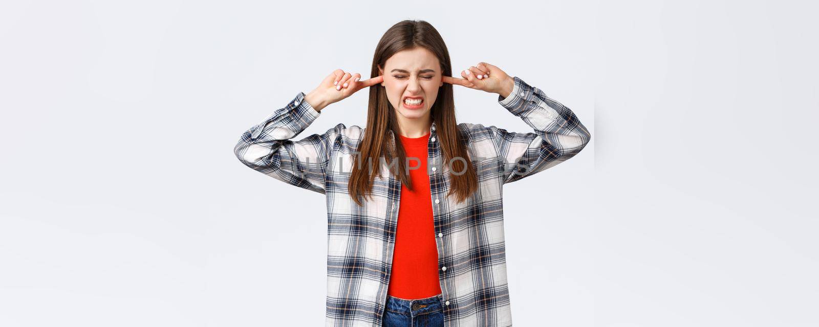 Lifestyle, different emotions, leisure activities concept. Girl cant stand this music. Displeased and bothered young female student shut ears with fingers and grimacing from loud annoying sound by Benzoix