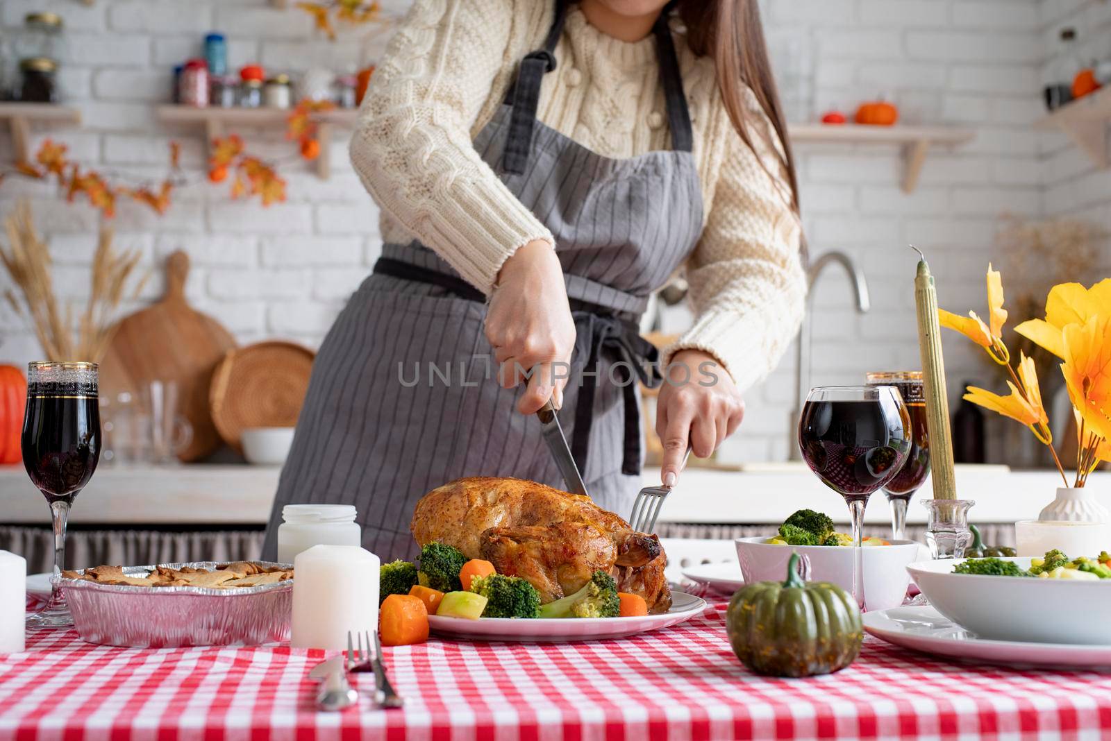 Woman in sweater and apron cutting turkey for family dinner at home kitchen by Desperada