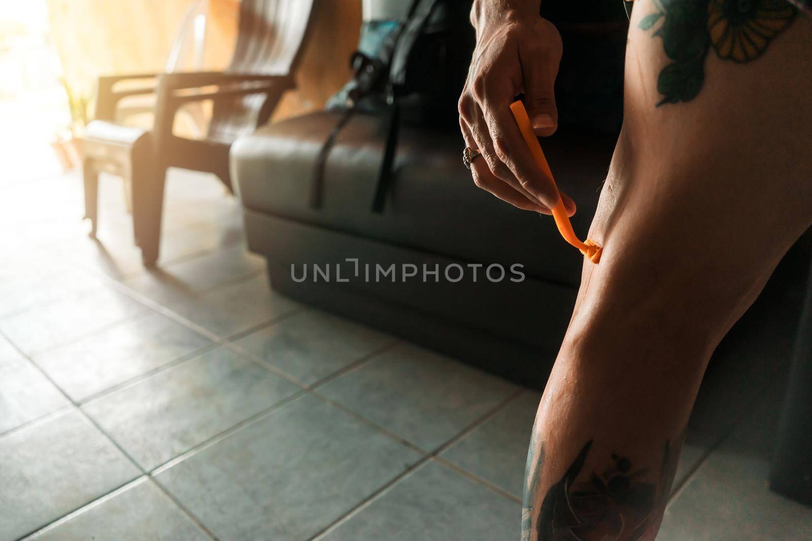 Closeup on the hand of a young Latin man shaving his leg before getting a tattoo by cfalvarez