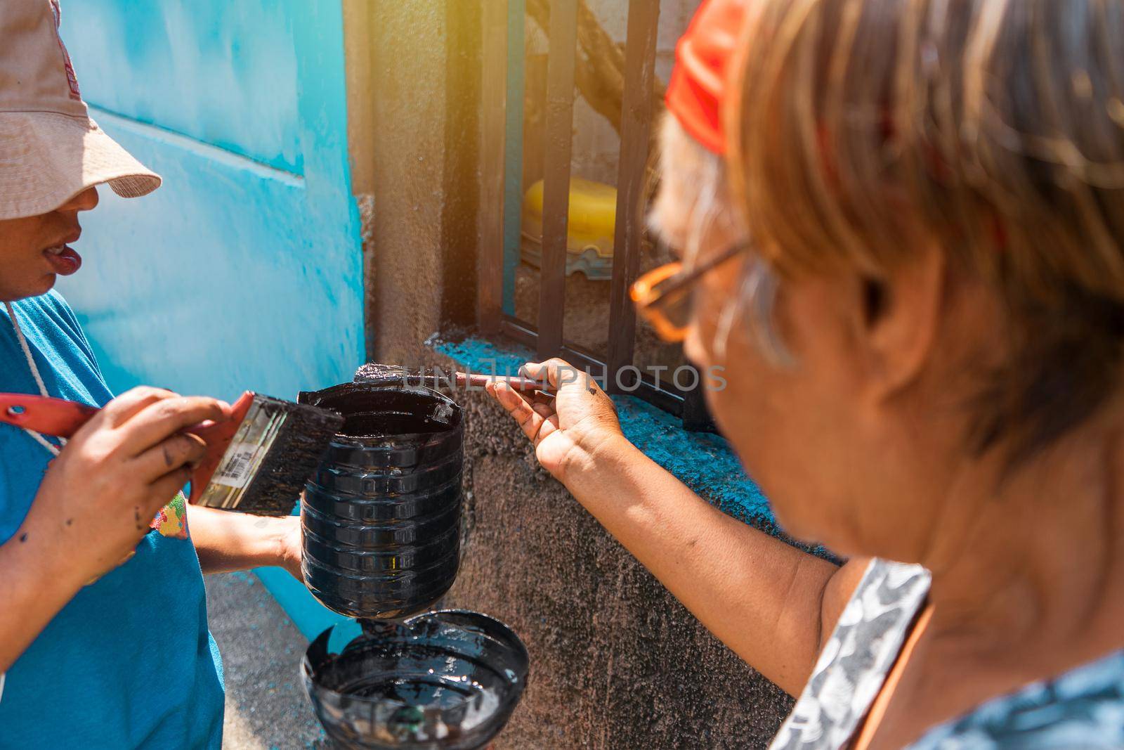 Latin mother and daughter loading paint in a plastic bucket working together to remodel their house by cfalvarez