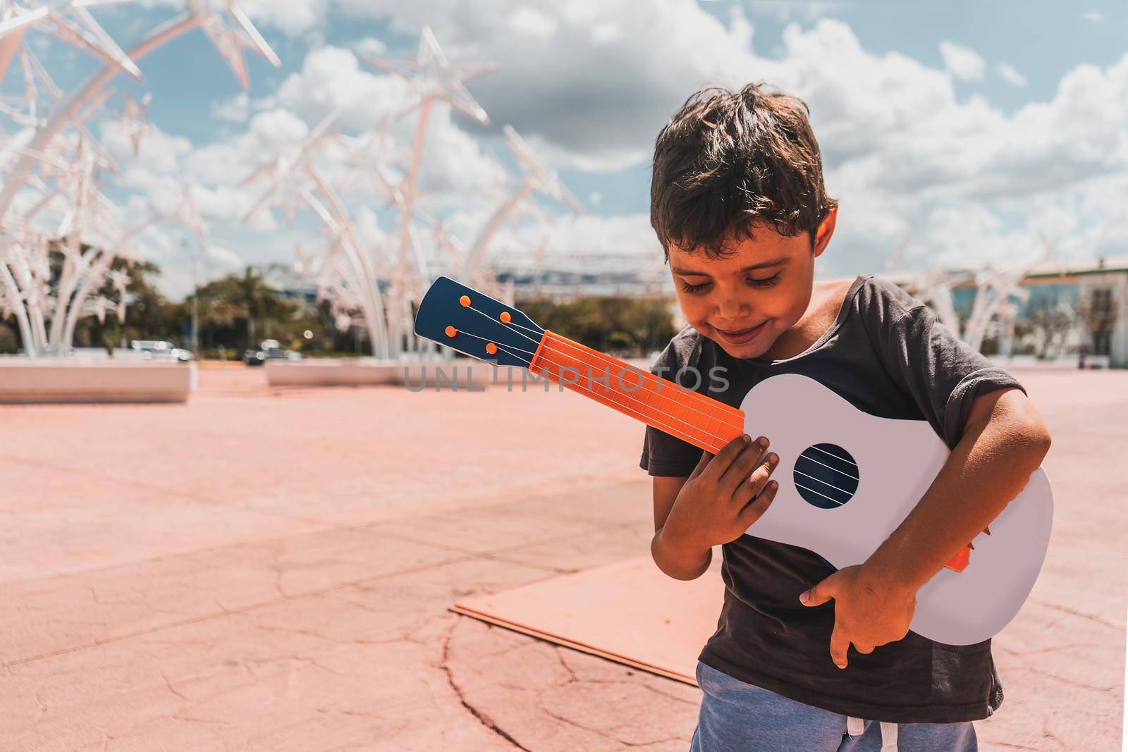 Moody photo of a Latino boy playing a ukulele in a public plaza by cfalvarez