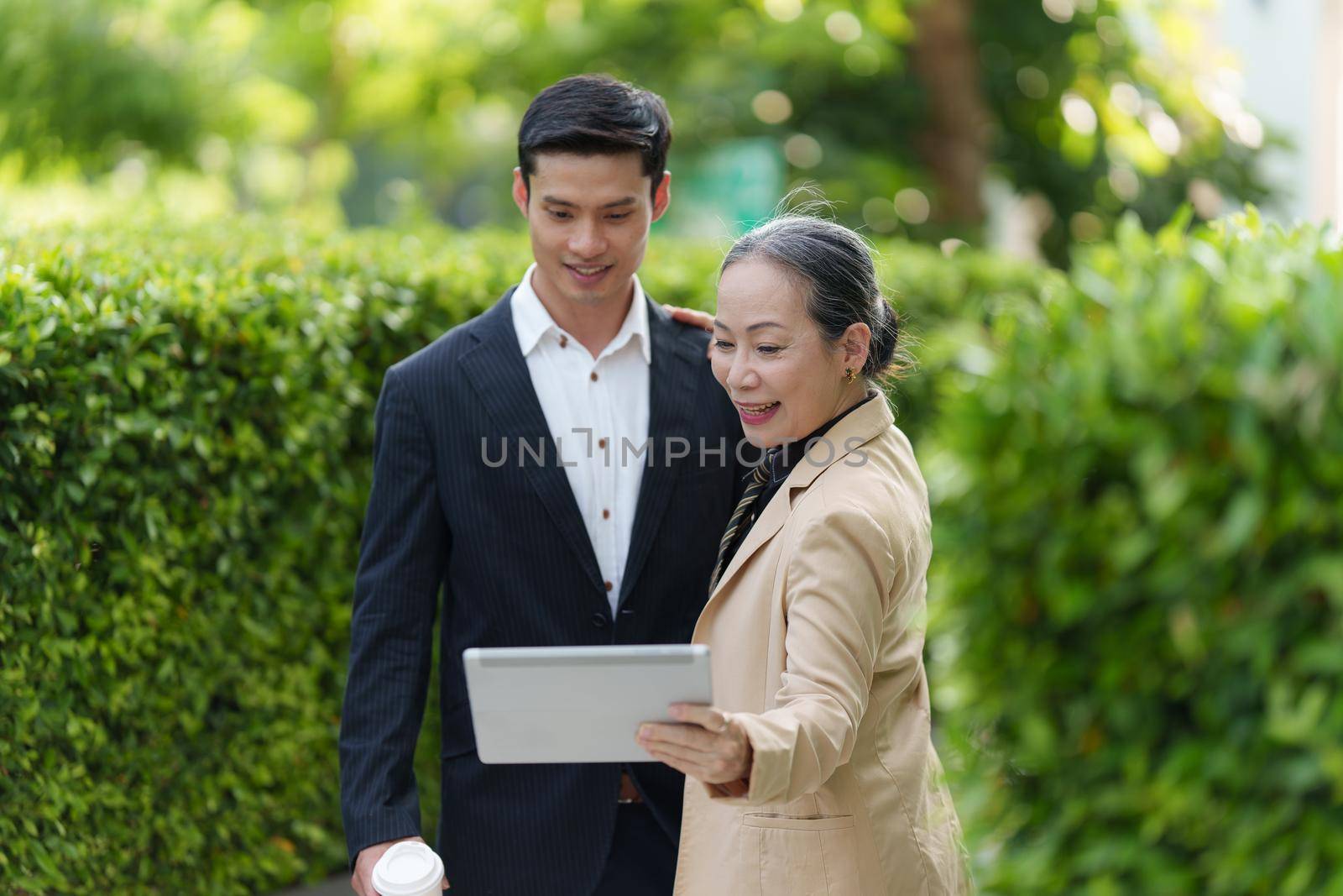 Portrait of Asian Senior Business woman and young business man discussing about project by digital tablet. Account and Finance concept