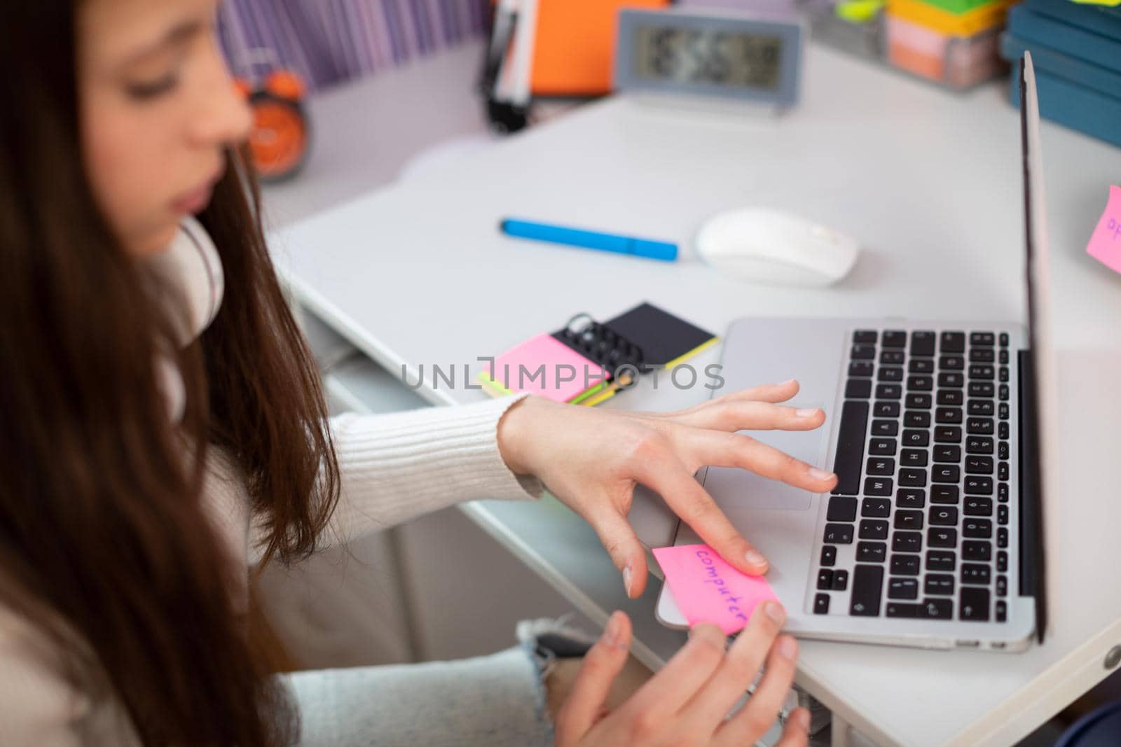 A modern method of learning English. A young brunette girl sticks a card that says computer on her laptop.