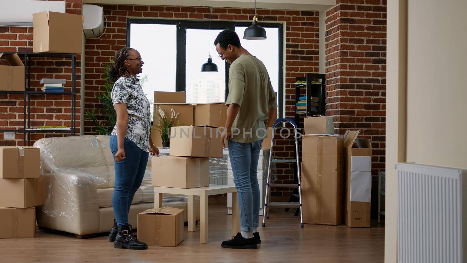 Husband and wife moving in new home with carton boxes, using furniture to start new beginnings together in living room. Holding packages in rented property on loan for relocation.