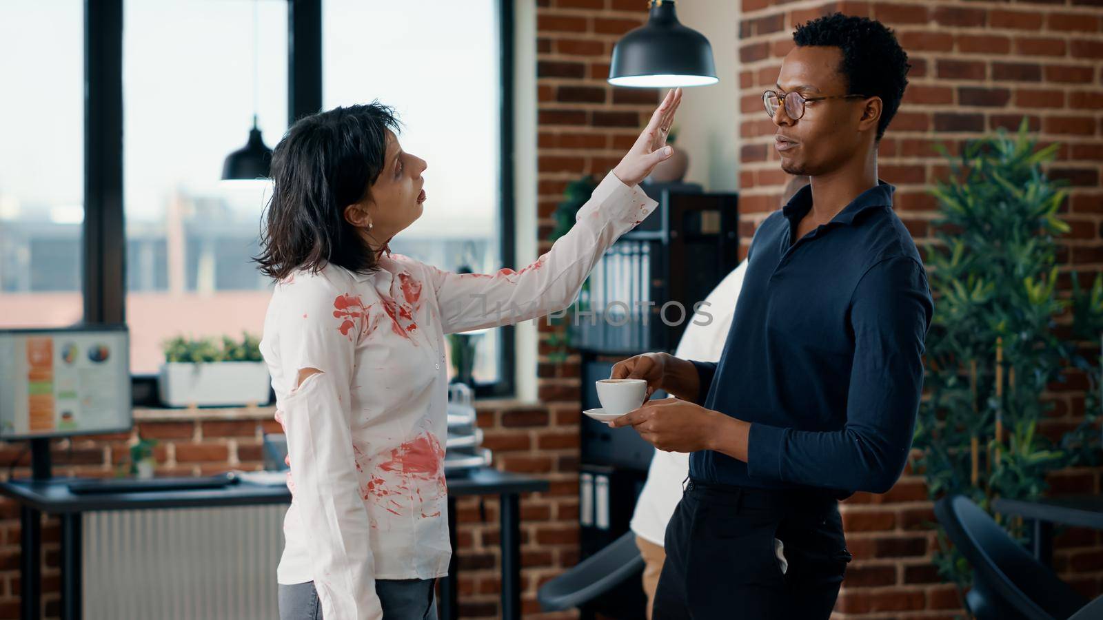 Brain dead zombie woman touching businessman while discussing. Doomsday survivor talking with dangerous dead walking corpse having bloody and deep wounds in office workspace.