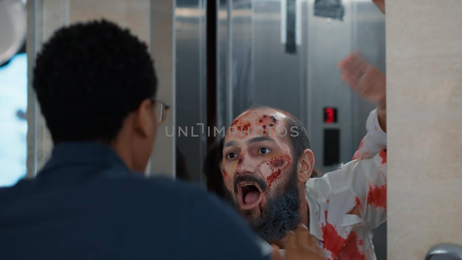 Confident man encountering evil zombies at elevator when leaving work. Horror looking undead monsters coming out of elevator and chasing doomsday survivor downstairs on building hallway.