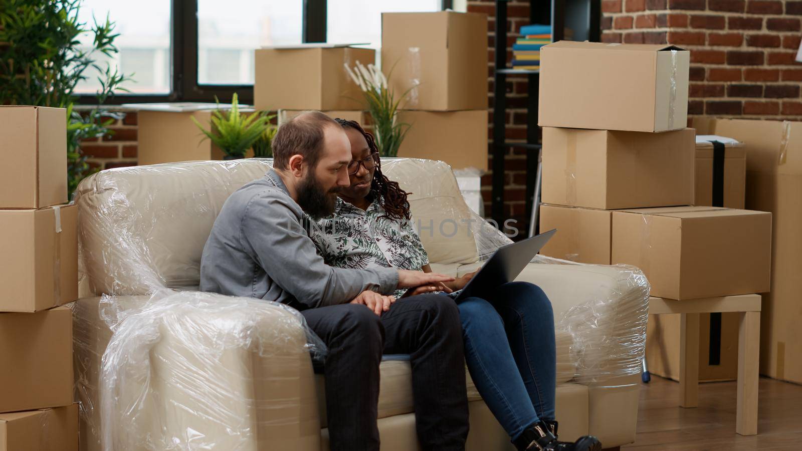 Married life partners using laptop to buy interior furniture, moving in new real estate apartment. Looking at decor inspiration on website to decorate living room together, new beginnings.