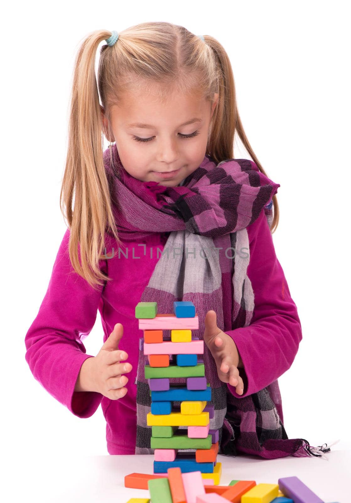 Children's hobbies, creativity, a little girl in a blue dress playing with the wood game jenga on white background by aprilphoto