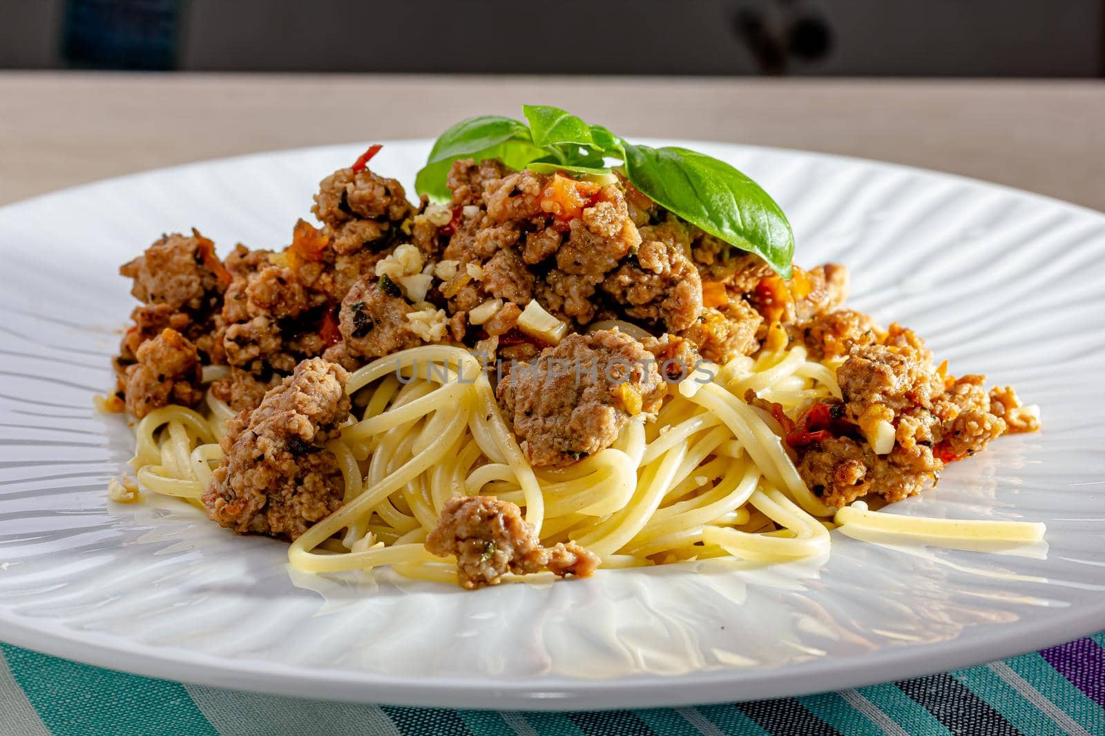 Rich spicy Italian spaghetti Bolognaise with parmesan cheese and a fresh green basil leaves viewed from overhead on a white plate in square format.