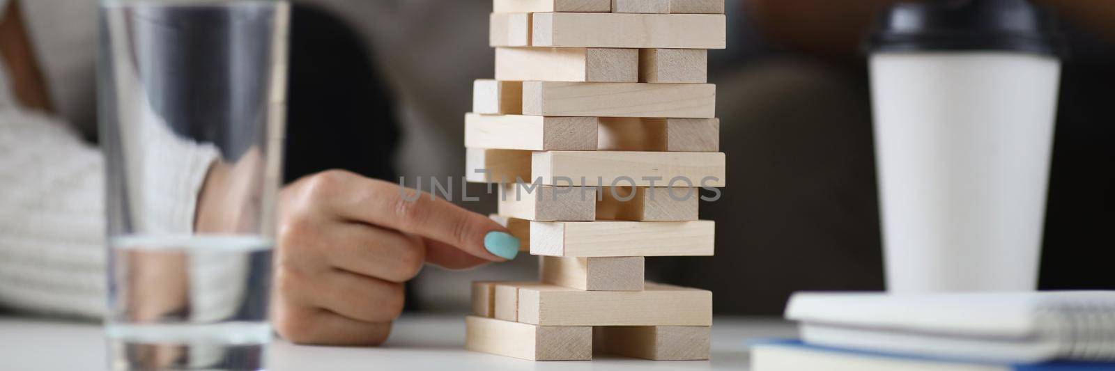 Close-up of womans hand pull one of wooden blocks from high build tower. Friends or colleagues play board game for fun. Entertainment, spare time concept