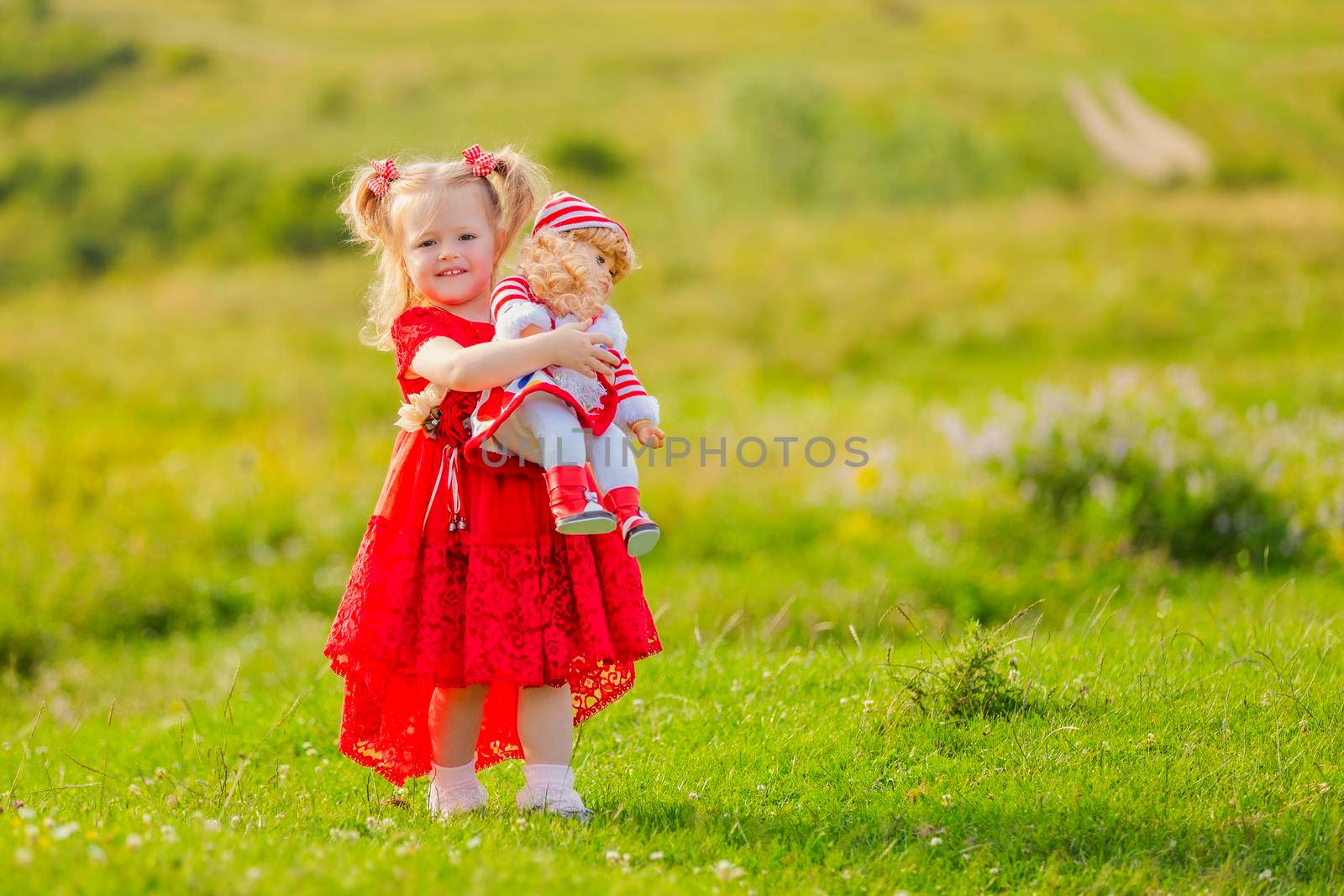 girl in a red dress and with a doll in her hands stands in nature