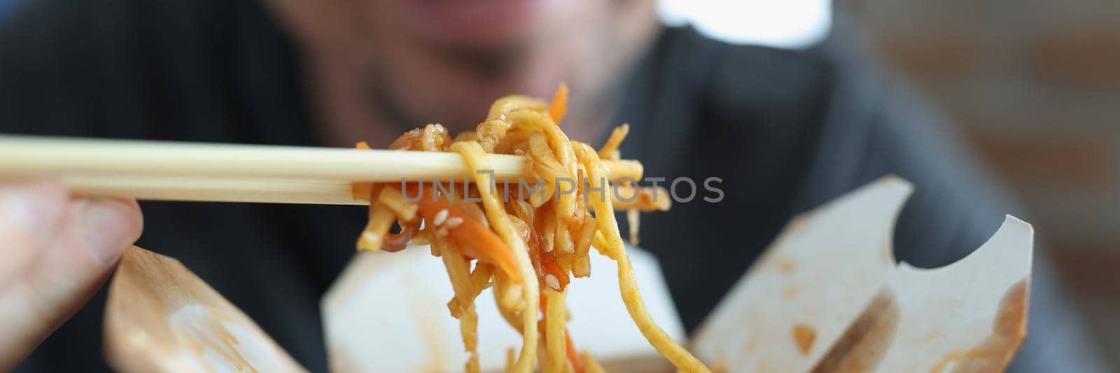 Smiling man eating spicy noodle chinese food with vegetable using chopsticks by kuprevich