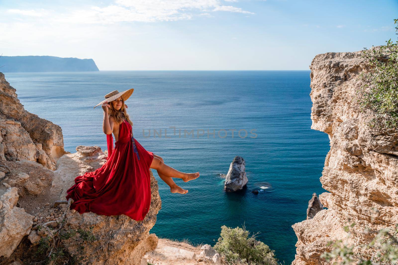 A girl with flowing hair in a long red dress sits on a rock above the sea. The stone can be seen in the sea