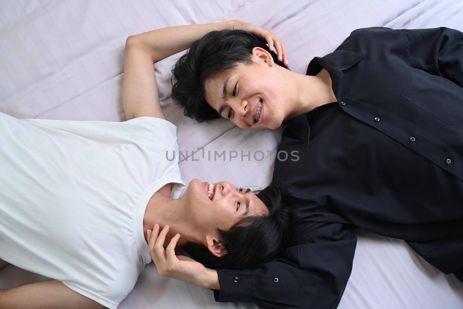 Overhead view young gay couple lying down on bed, spending time together. LGBT, pride, relationships and equality concept.