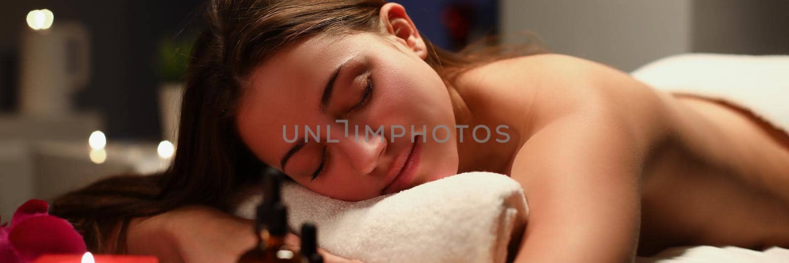 Portrait of young woman laying with closed eyes on massage table in spa. Lady get total relaxation in luxury spa centre. Massage, wellness, care concept