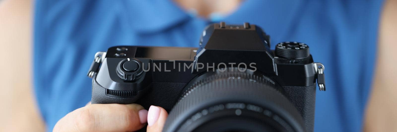 Close-up of woman photographer in blue outfit with camera in her hands in photo studio. Professional artist hold new model of photocamera. Creative concept