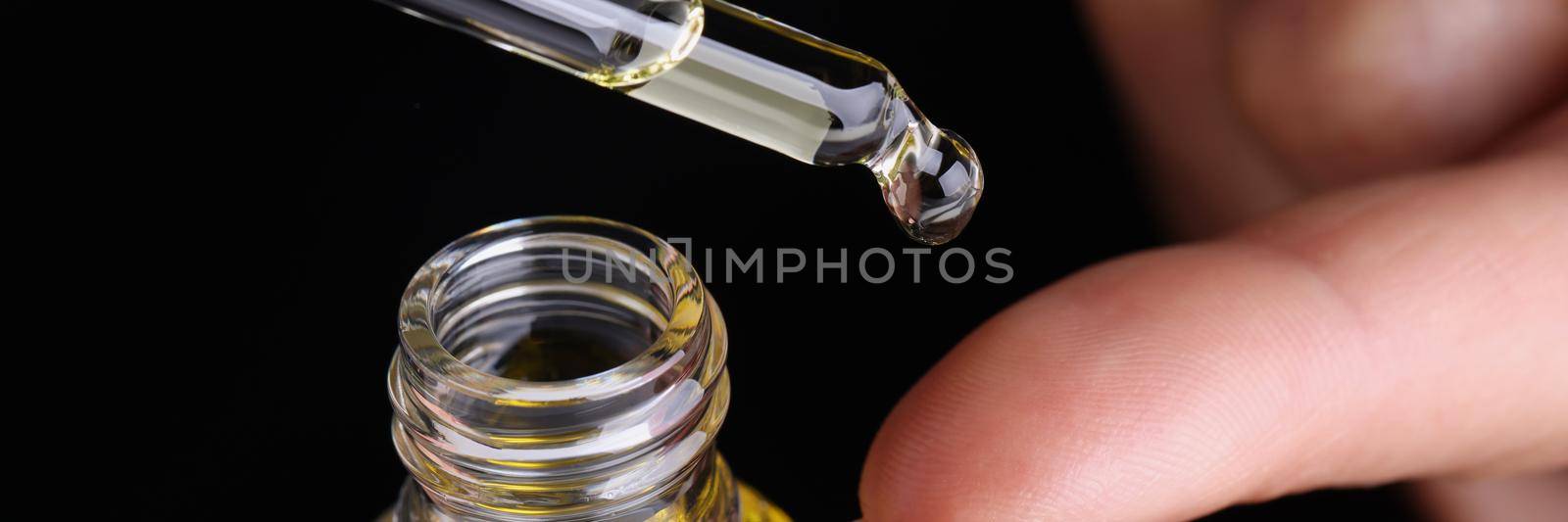 Person dripping drop of extract oil on finger with eyedropper by kuprevich