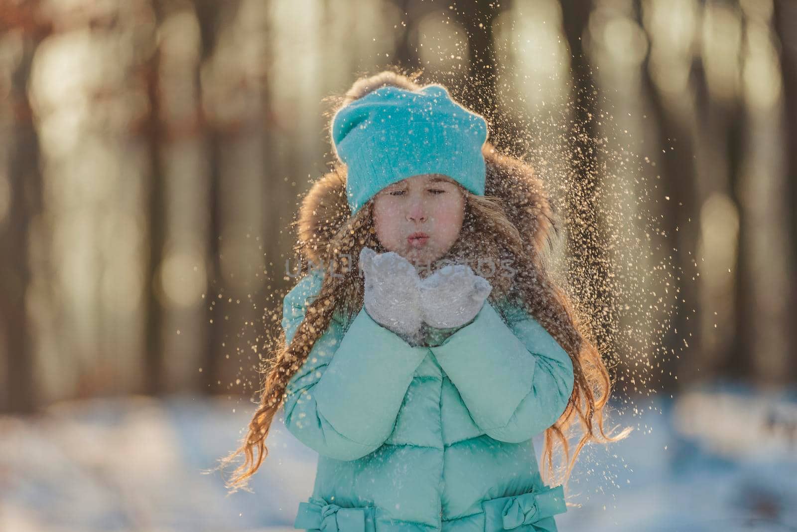 little girl blows on the snow that is on her mittens