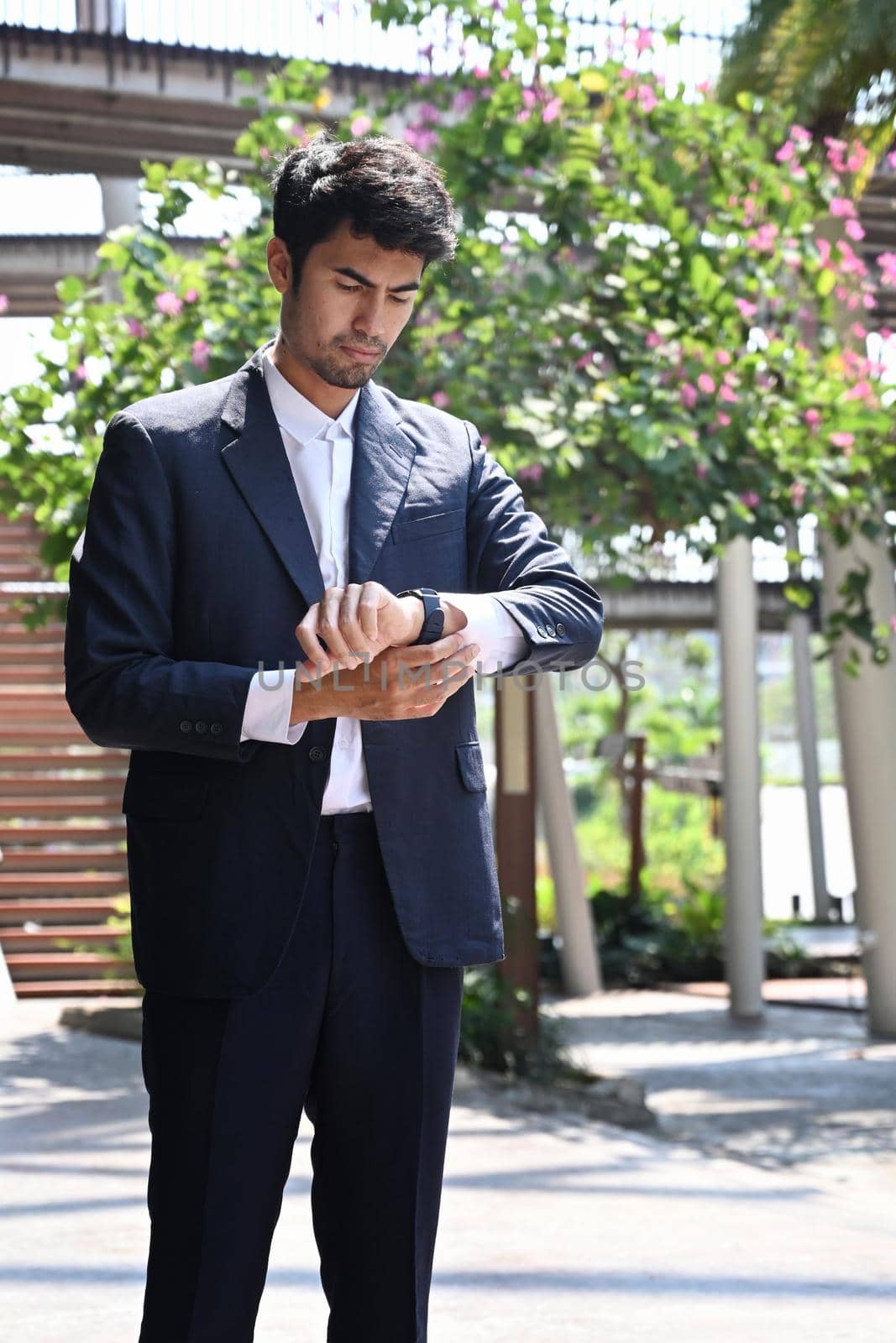 Elegant businessman checking time on his wrist watch while standing on city street.