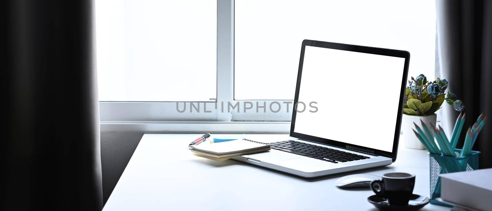 Laptop computer, potted plant, coffee cup and book on white table at comfortable home. by prathanchorruangsak