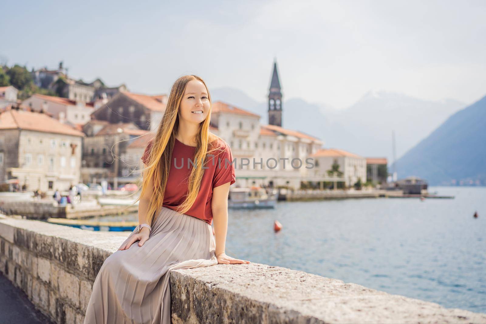 Woman tourist enjoying Colorful street in Old town of Perast on a sunny day, Montenegro. Travel to Montenegro concept. Scenic panorama view of the historic town of Perast at famous Bay of Kotor on a beautiful sunny day with blue sky and clouds in summer, Montenegro, southern Europe.