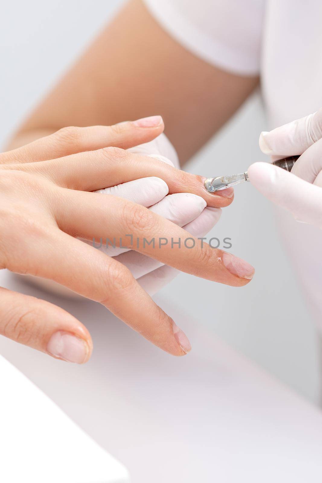 Hands of manicurist pushing cuticles on female's nails with manicure tool. Woman receiving manicure and nail care procedure