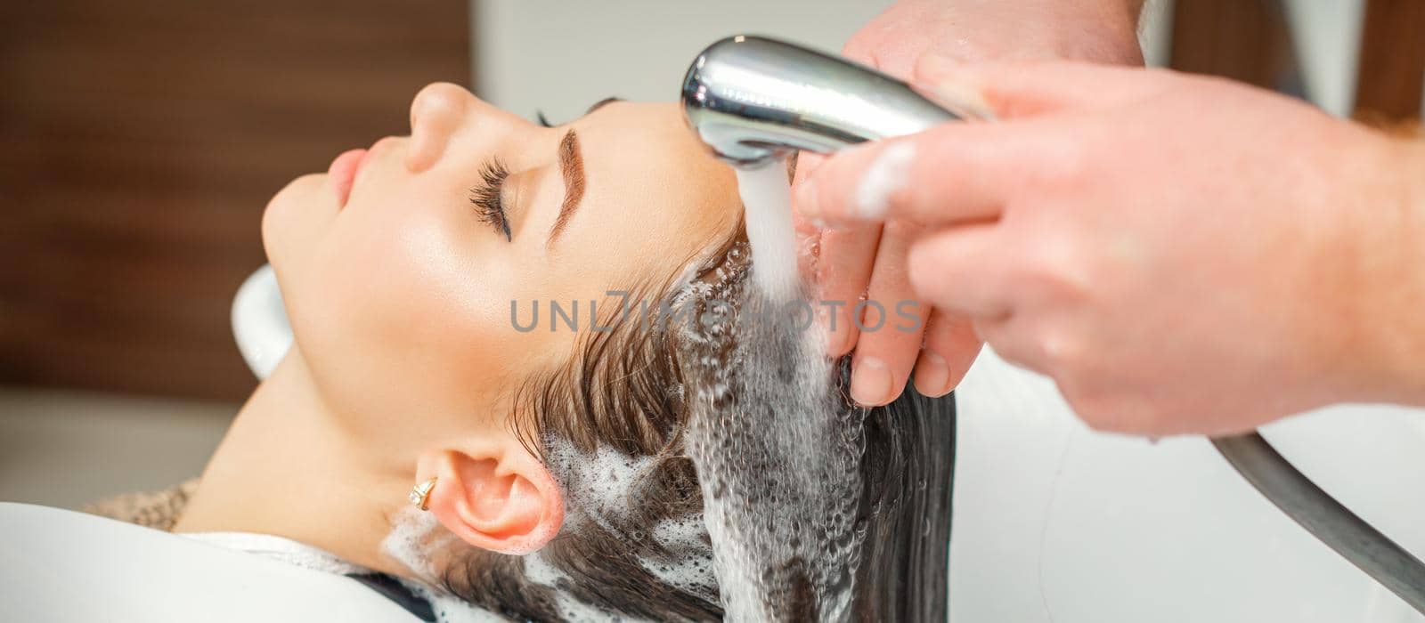 Close up of hands of hairdresser washing hair of woman in sink at beauty salon