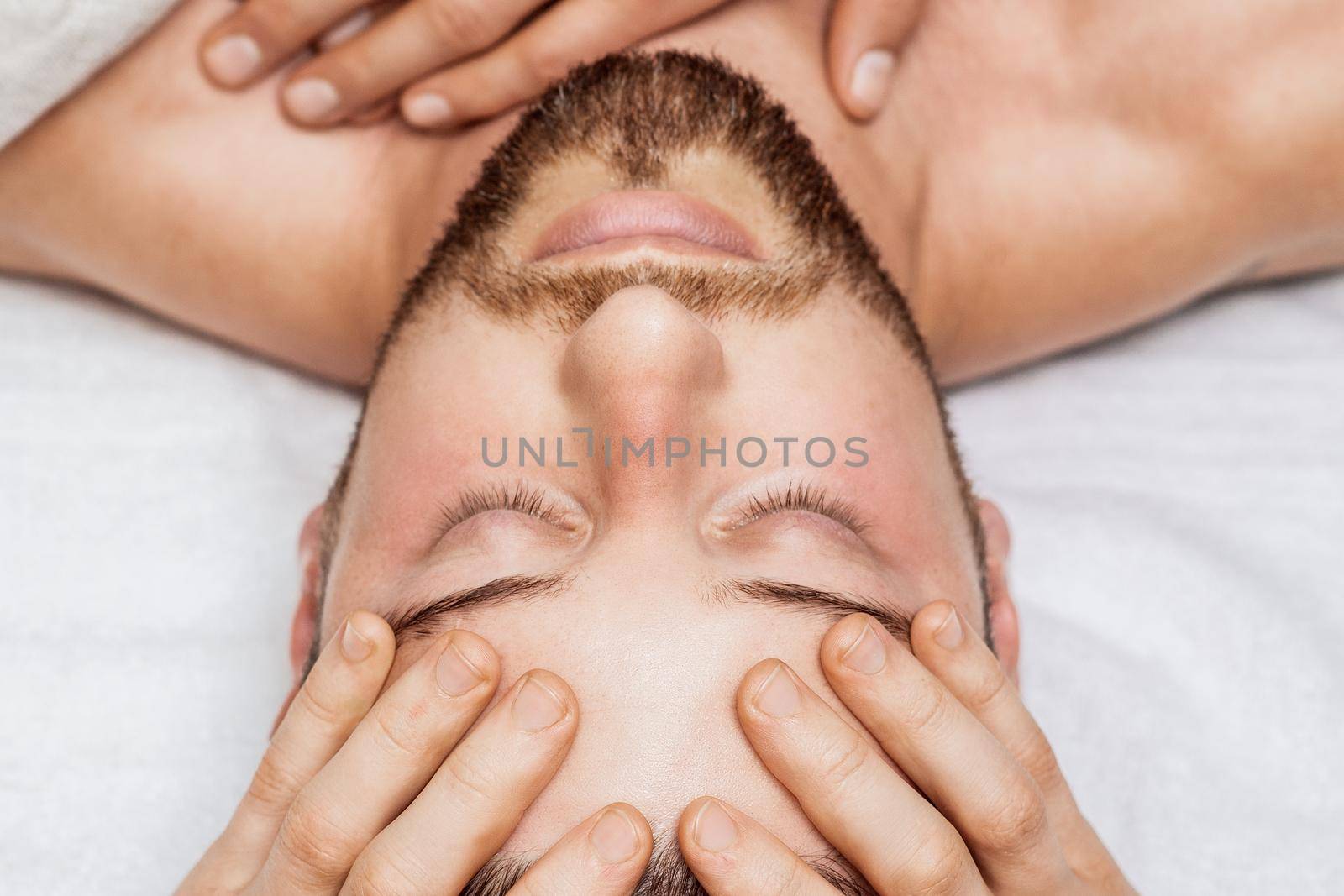 Handsome young man receiving relaxing head massage from a two masseurs in four hands in a health spa center