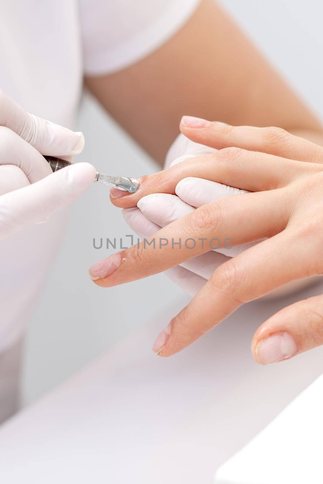 Hands of manicurist pushing cuticles on female's nails with manicure tool. Woman receiving manicure and nail care procedure