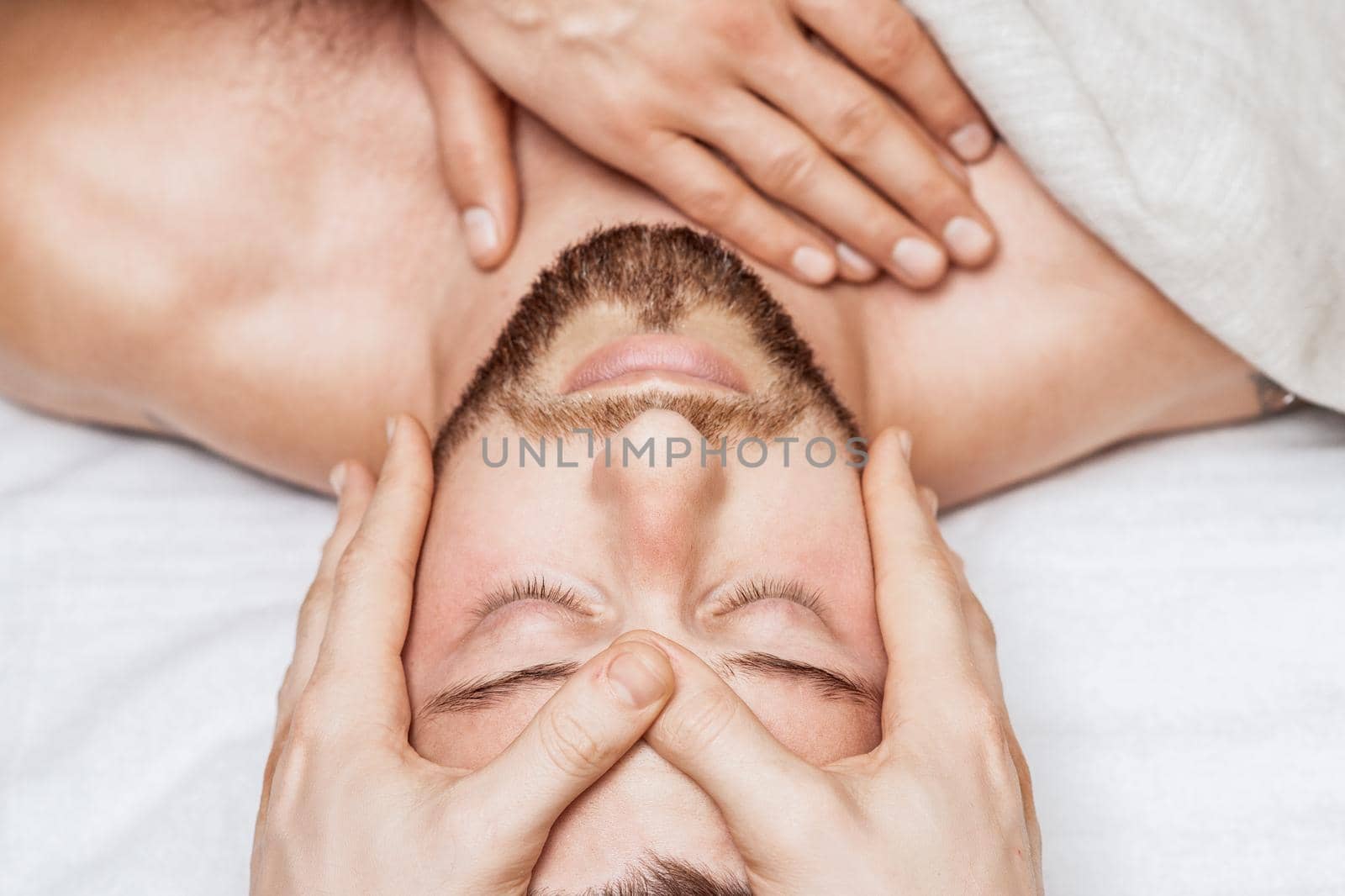 Top view of relaxing young caucasian man enjoying head massage by two masseurs