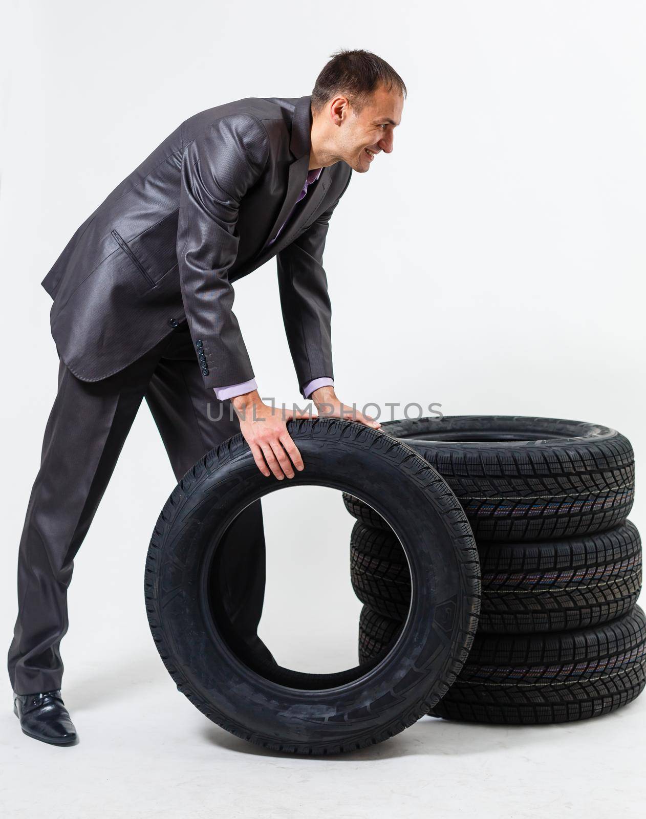 Full length portrait of a young businessman leaning on a pile of car tires isolated on white background