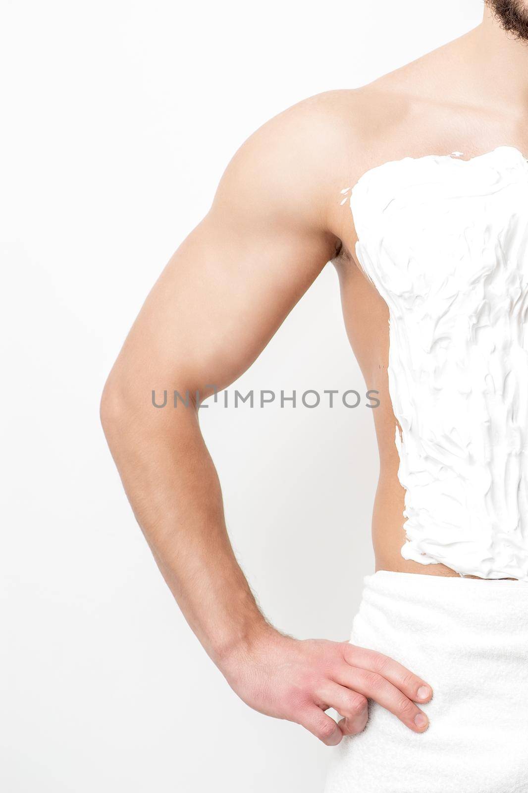 Young caucasian man with beard holds razor shaves his chest with white shaving foam on white background. Man shaving his torso
