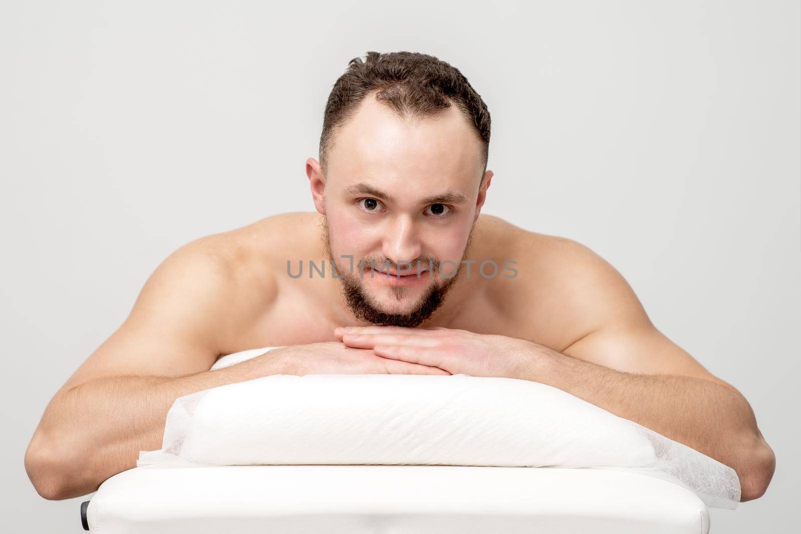 Young caucasian man lying on front on table spa, waiting for beauty treatment and looking at camera