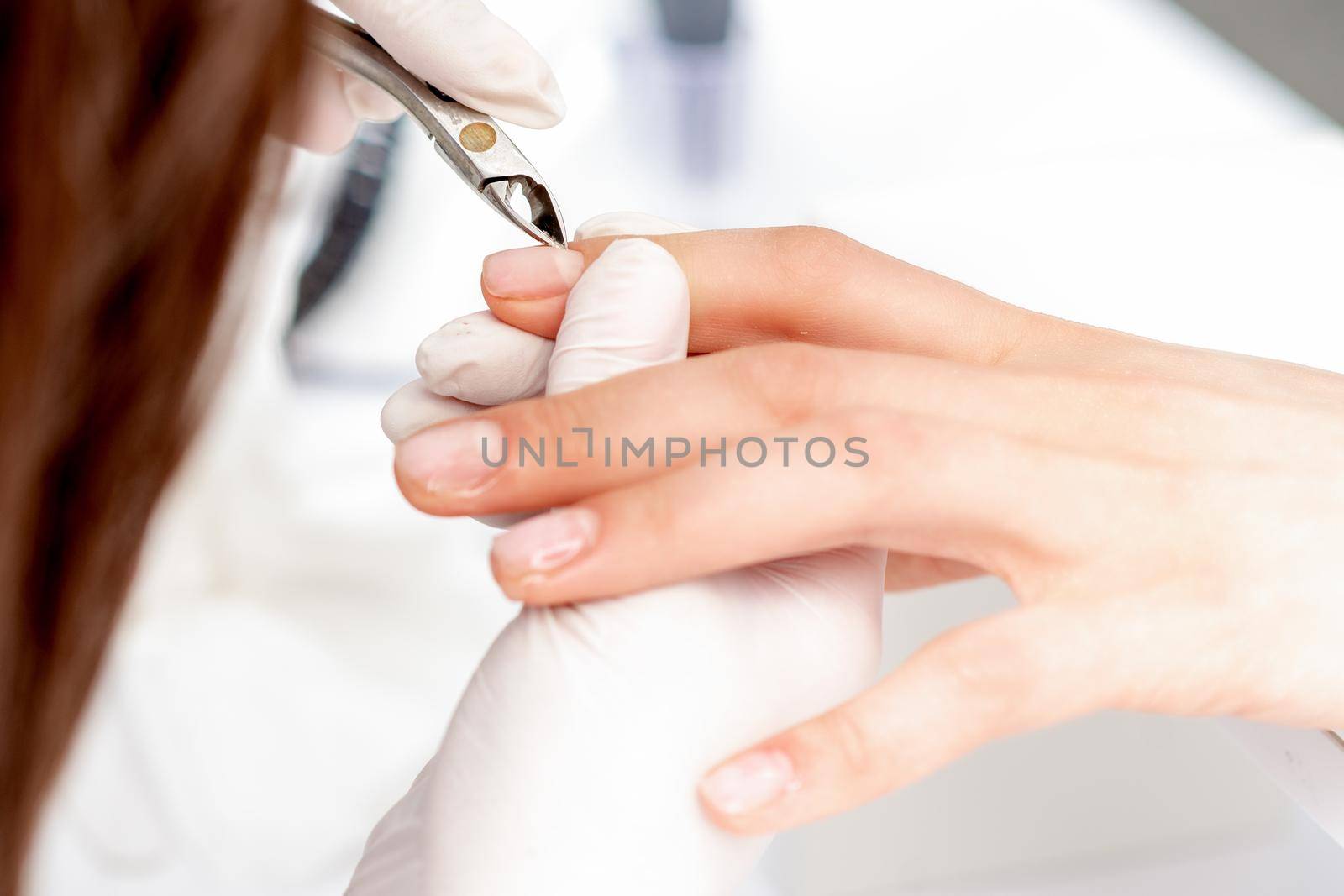 Close up of manicurist using manicure clipper to remove cuticle of female nails in manicure salon