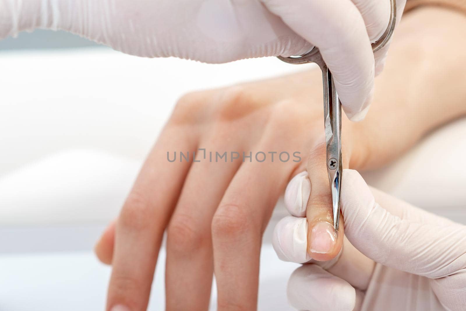 Close up of manicurist using manicure scissors to remove cuticle of female nails in manicure salon