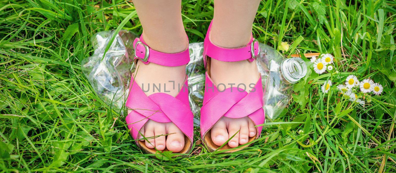 Legs of a little girl tramples a plastic bottle on the green grass in the park