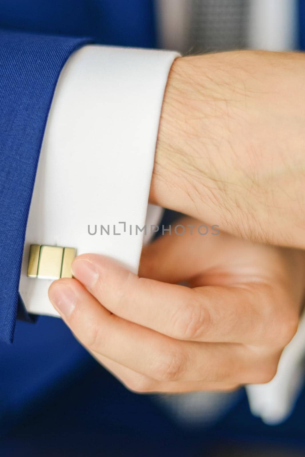 Groom or businessman fasten cufflink on the cuff of the shirt wearing blue suit. Soft focus