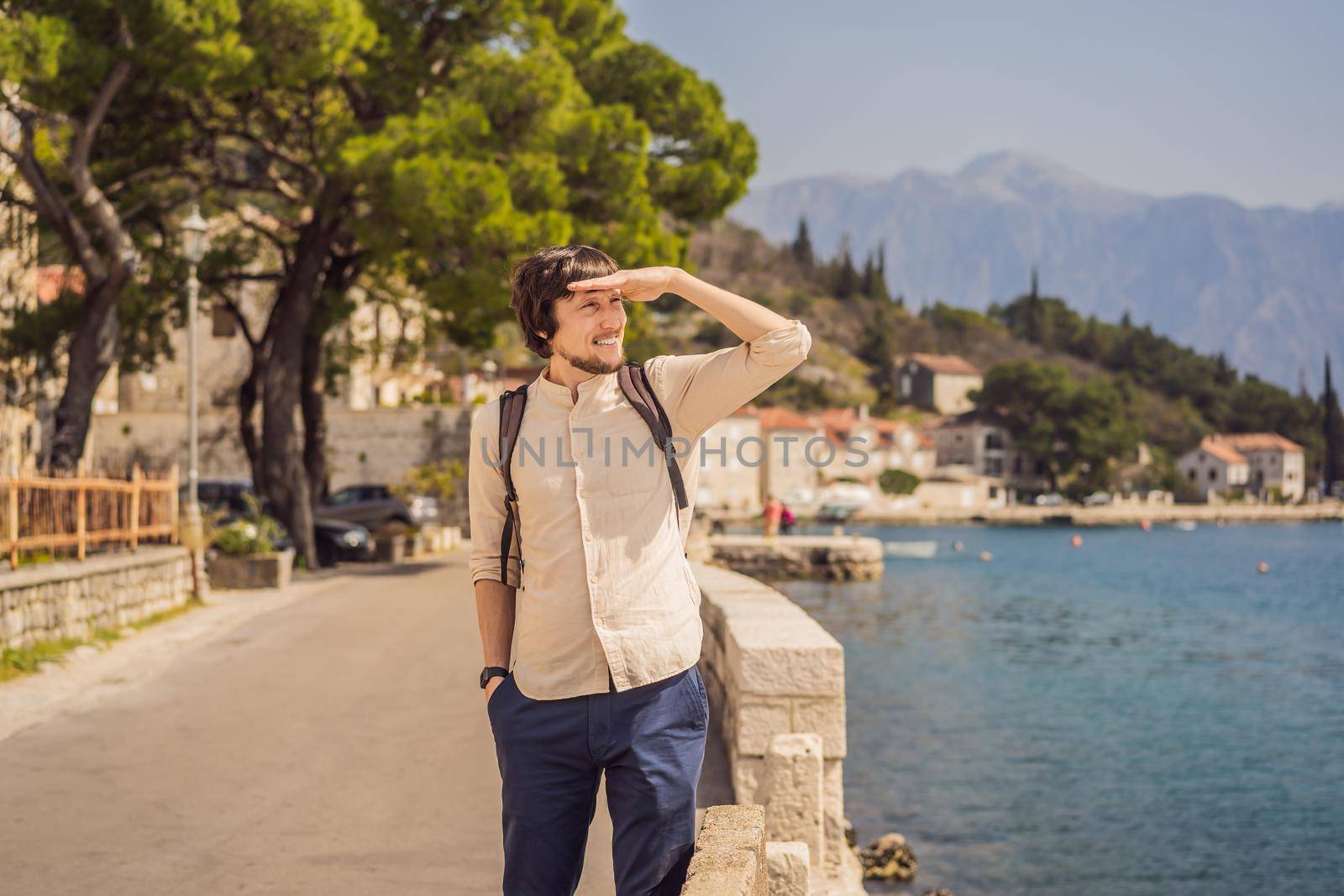Man tourist enjoying Colorful street in Old town of Perast on a sunny day, Montenegro. Travel to Montenegro concept. Scenic panorama view of the historic town of Perast at famous Bay of Kotor on a beautiful sunny day with blue sky and clouds in summer, Montenegro, southern Europe.